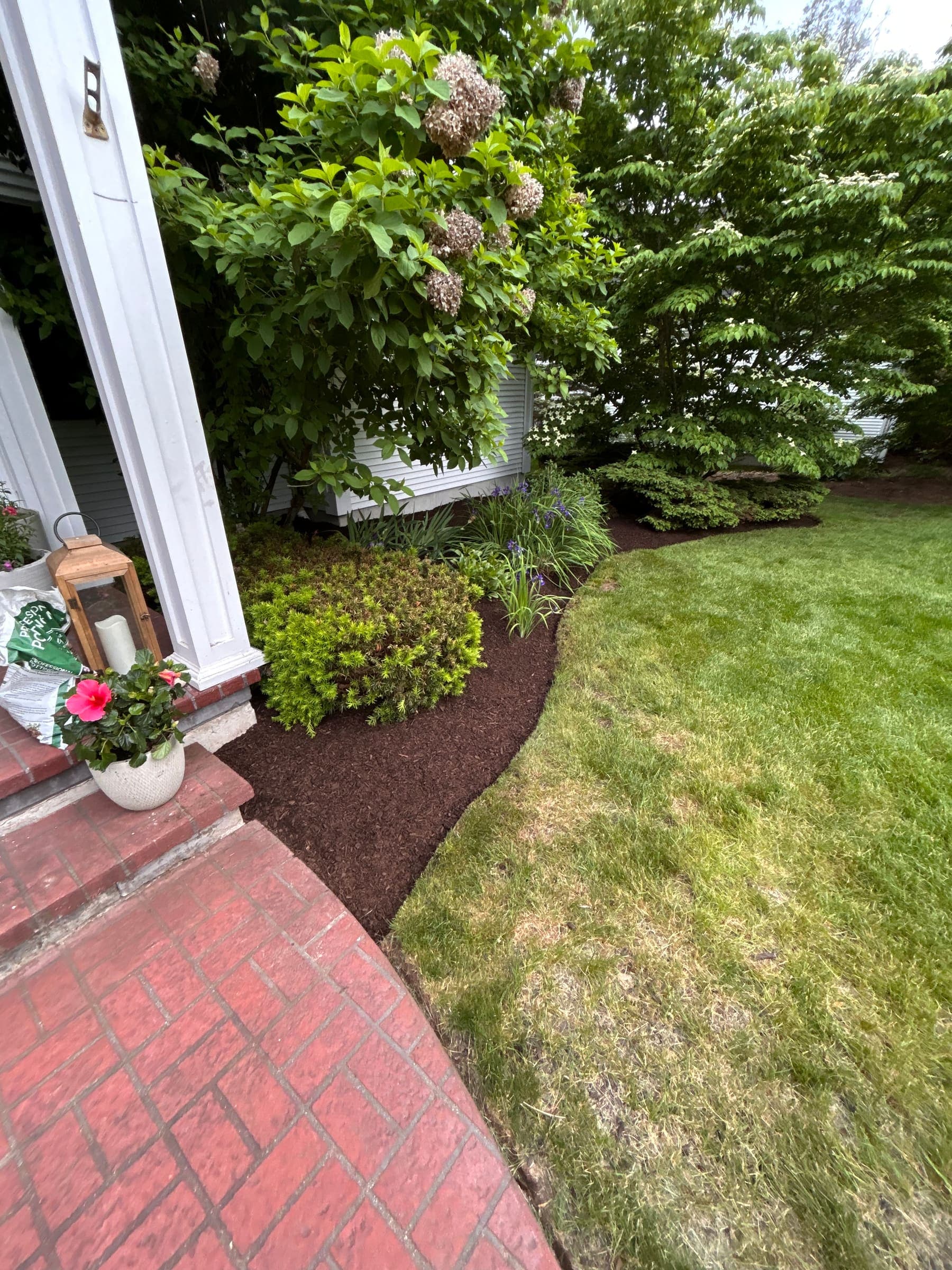 Trimmed shrubs and fresh mulch edged against a brick patio beside a Connecticut home